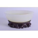 A GOOD 19TH CENTURY CHINESE CARVED GREEN HARDSTONE BOWL Qing, possibly jade, upon a hardwood base.