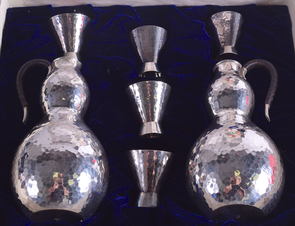 A CASED JAPANESE TAISHO PERIOD HAMMERED SILVER SAKE SET comprising of two jugs & five cups. 300