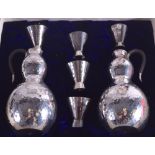 A CASED JAPANESE TAISHO PERIOD HAMMERED SILVER SAKE SET comprising of two jugs & five cups. 300
