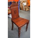 AN EARLY VICTORIAN MAHOGANY HARD SEAT HALL CHAIR, with carved shield back decoration on turned and