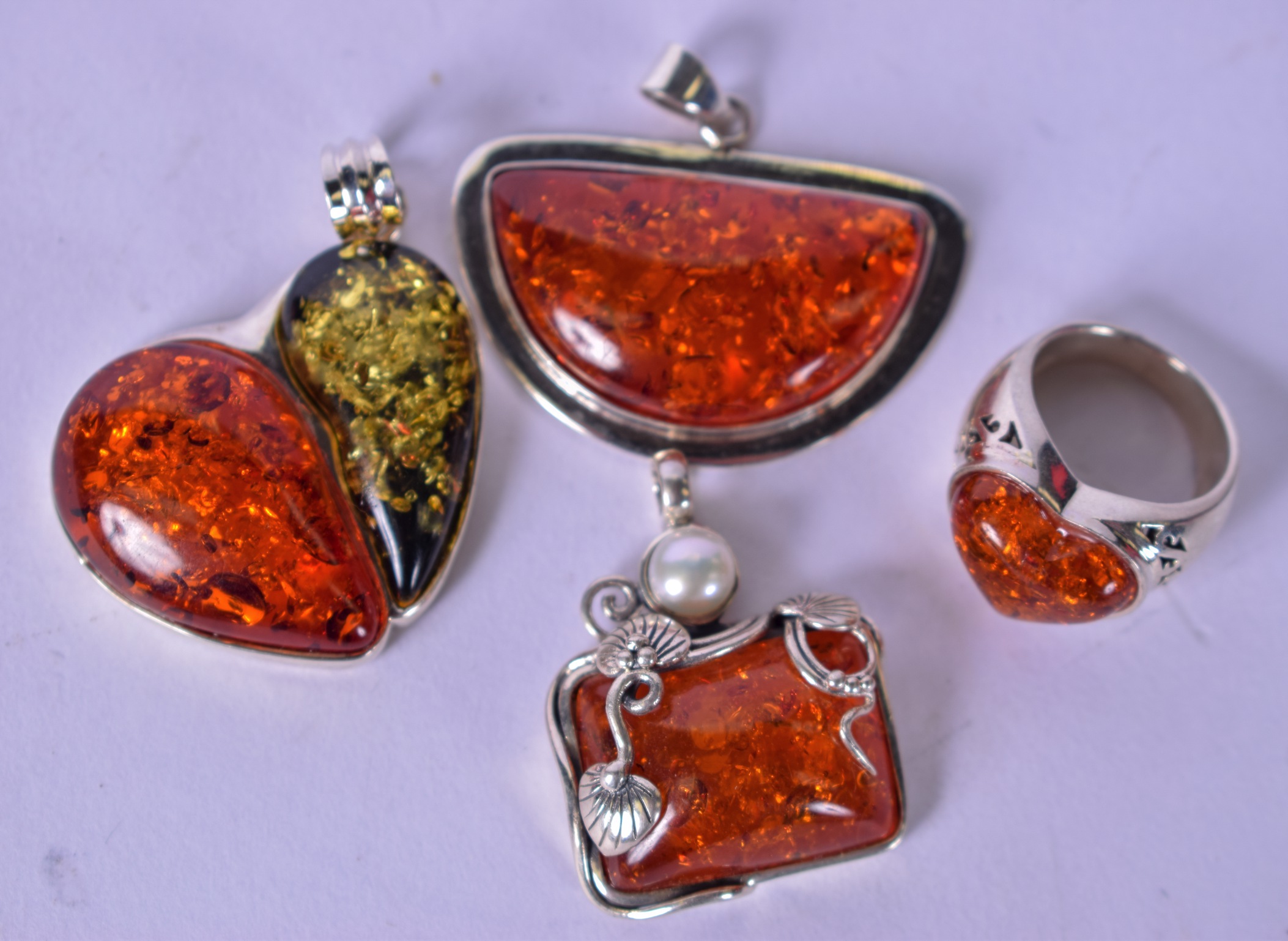 AN AMBER TYPE HEART SHAPED RING, together with three silver mounted pendants. (4)