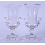 A PAIR OF EARLY 20TH CENTURY TWIN HANDLED GLASS VASES OR URNS, formed on square plinths. 22 cm high.