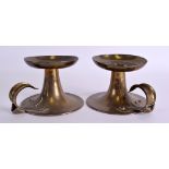 A PAIR OF ARTS AND CRAFTS BRASS CHAMBERSTICKS Attributed to Liberty & Co, with scrolling handles. 15