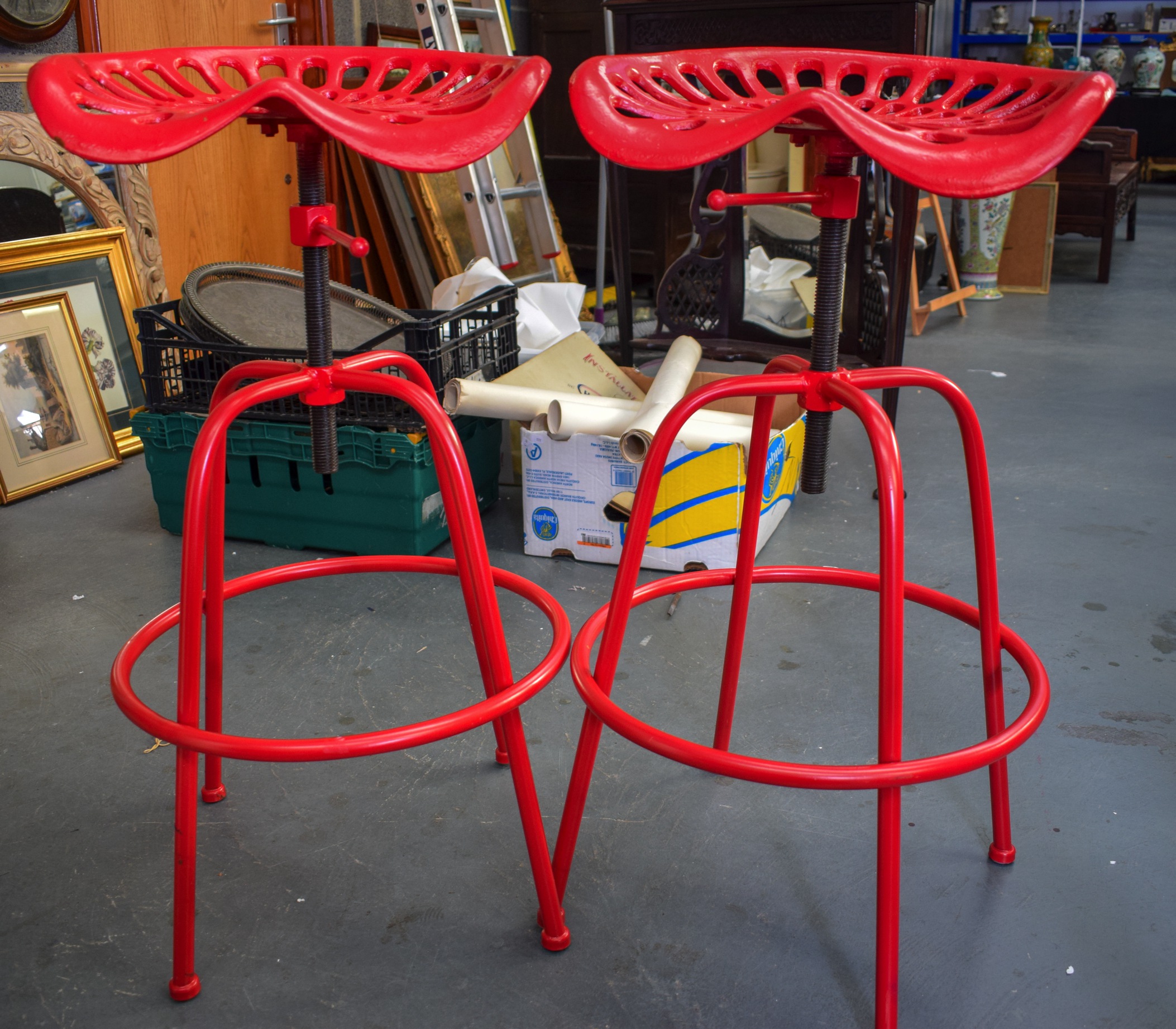 A STYLISH PAIR OF TRACTOR SEAT STOOLS, painted red. 84 cm high.