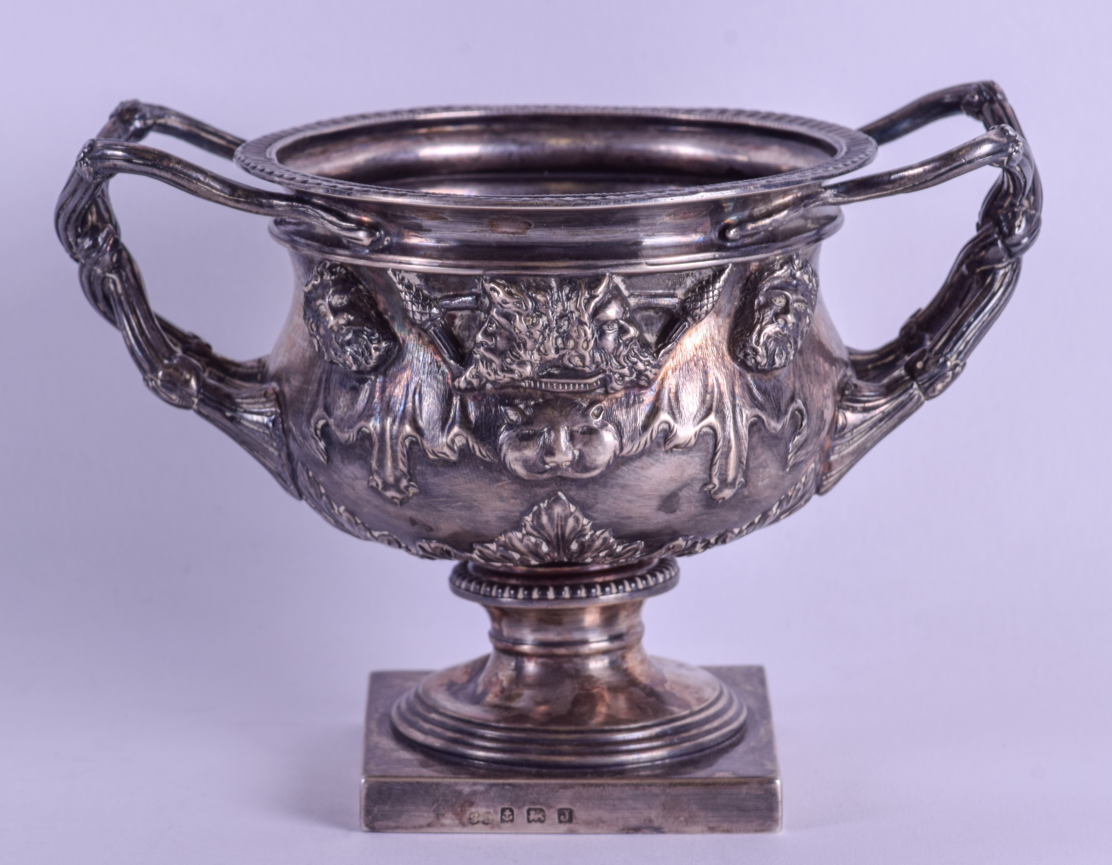 AN ENGLISH SILVER TWIN HANDLED WARWICK VASE decorated with classical figures upon a pedestal base.