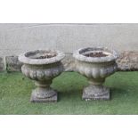 A PAIR OF COMPOSITION STONE URNS, the lobed bowl with plain rim, on waisted socle and square base,