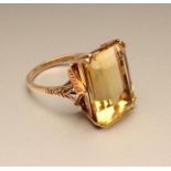 A CITRINE COCKTAIL RING, the rectangular cut stone claw set to open leaf shoulders and a plain 9ct