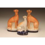 A PAIR OF VICTORIAN STAFFORDSHIRE POTTERY GREYHOUNDS, seated with free modelled fore-legs on oval