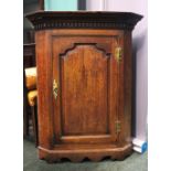 AN OAK HANGING CORNER CUPBOARD, straight fronted, with fluted cornice over a carved panel door,