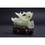 A CARVED PIECE OF JADE IN THE FORM OF A BIRD HOLDING A FLOWER IN ITS BEAK, sitting on a carved