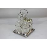 A silver plated four-piece glass cruet set with central loop handle, on square base with ball