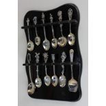 A collection of twelve silver, white metal and other commemorative spoons, on wooden display