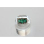 An emerald and diamond ring, claw set with three emeralds and an eight diamond border (two loose