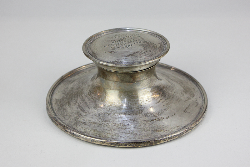 A George V silver capstan inkwell on loaded circular base, with engraved presentation inscription (