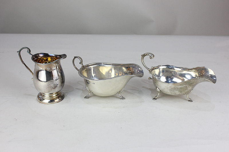 A George V silver sauce boat with flying scroll handle and scalloped border, on three hoof feet,