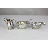 A George V silver sauce boat with flying scroll handle and scalloped border, on three hoof feet,