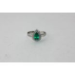 An emerald and diamond ring the pear shaped stone within a two row border of tiny diamonds in 18ct