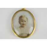 A 19th century oval miniature portrait of an infant, in a white shirt, on ivory, in glazed gilt