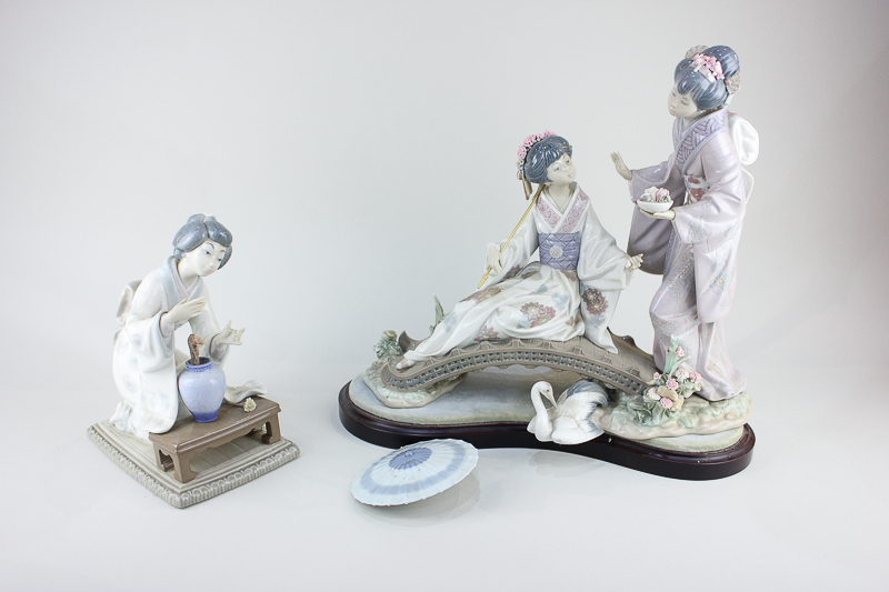 A Lladro figure group of two Japanese women, one seated on a bridge with stand (a/f - parasol