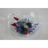 A clear glass leaf shaped bowl containing a collection of glass confectionary, one sweet with