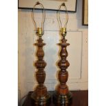 A pair of wooden baluster table lamps on circular metal bases, with cream coloured shades, 77cm (a/f