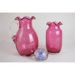 A Victorian cranberry glass jug, a similar vase and a clear glass paperweight with controlled bubble