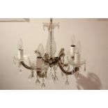 A modern glass chandelier with five scroll branches, central baluster stem, swags and drops,