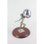 A silver plated female nude figure holding a ball containing an inkwell, on circular wooden base,