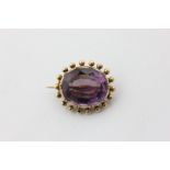 An amethyst brooch, the oval cut stone in a beaded mount