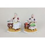 A pair of Continental porcelain seated figures of women, one with a dog on her lap, the other with a