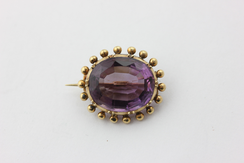 An amethyst brooch, the oval cut stone in a beaded mount