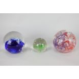 Three glass paperweights, one with green frond and controlled bubbles, one blue with bubbles, and