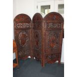 An Indian carved hardwood three-panel room screen, heavily decorated with foliage, flowers and