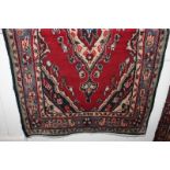 A Persian style wool rug, red field, with central diamond motif within multiguard border, 124cm by