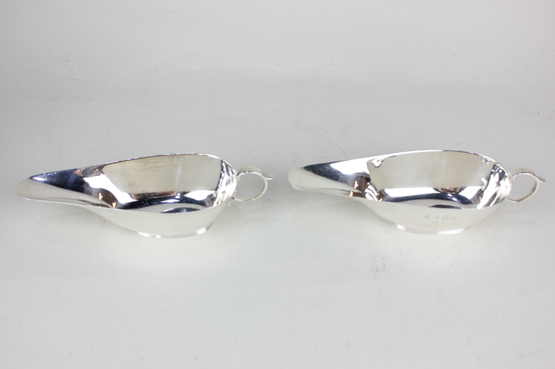 A pair of George VI silver sauce boats with scroll handles on reeded bases, engraved initials and