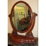 A large Victorian mahogany oval framed dressing table mirror with foliate carved supports, on curved