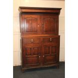 A George III oak cupboard with cornice and drop finials above two carved panel doors, two drawers