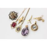 An 18ct compass pendant, gold revolver charm, bellows charm, an amethyst pendant, a red stone