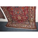 A Persian style wool rug, red field, with central stylized floral motif within multiguard border,