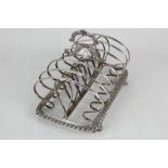A George IV silver toast rack, six scroll divisions with central handle and gadrooned base, on