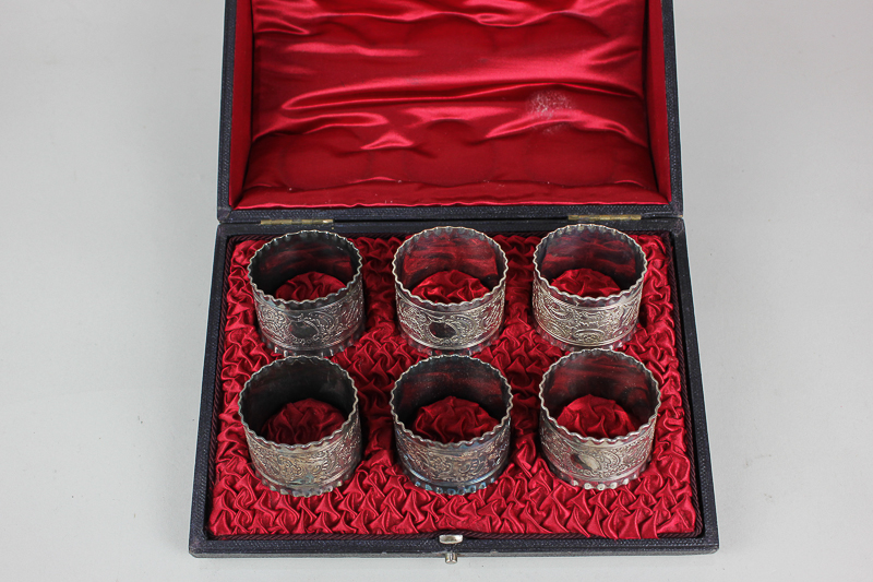 A cased set of six silver plated napkin rings cast with scroll decoration and frilly border, in