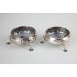 A pair of George III silver cauldron salts with embossed floral decoration, on three hoof feet,