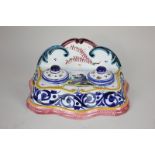 A French Quimper faience desk stand with two inkwells and covers, decorated with seated figure and