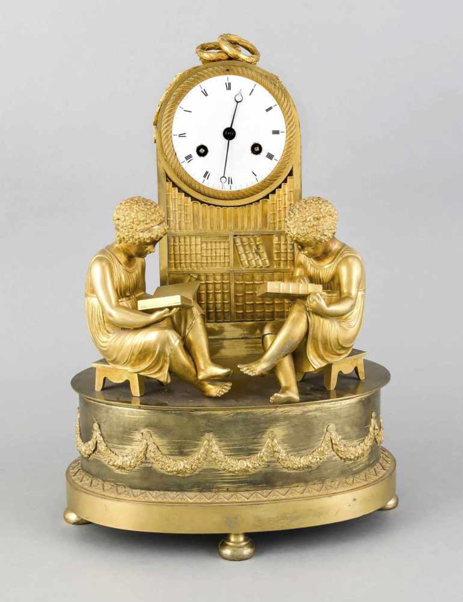 Lectura-Pendule, um 1820, feuervergoldete Bronze, ovaler gestufter Sockel, darauf montiert zwei