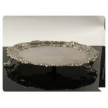 A WHITE METAL PIE CRUST EDGE SALVER WITH SCROLL AND FLOWER RIM, ON TRIPOD SCROLLED FEET,