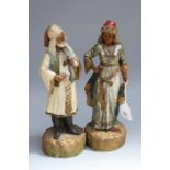 A pair of late 19th century German earthenware figures of Turks, he stands holding a pipe and she