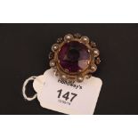 A Victorian amethyst glass brooch, the large circular amethyst glass in raised claw mount above a