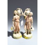 A pair of Royal Dux figures, a young man and female companion each carrying amphora on a
