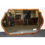 An Edwardian mahogany and parcel gilt wall mirror of cartouche shape with cushion frame and plain