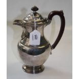 A silver hot water jug, baluster form with foliate borders and leaf mounted spout, wooden scroll